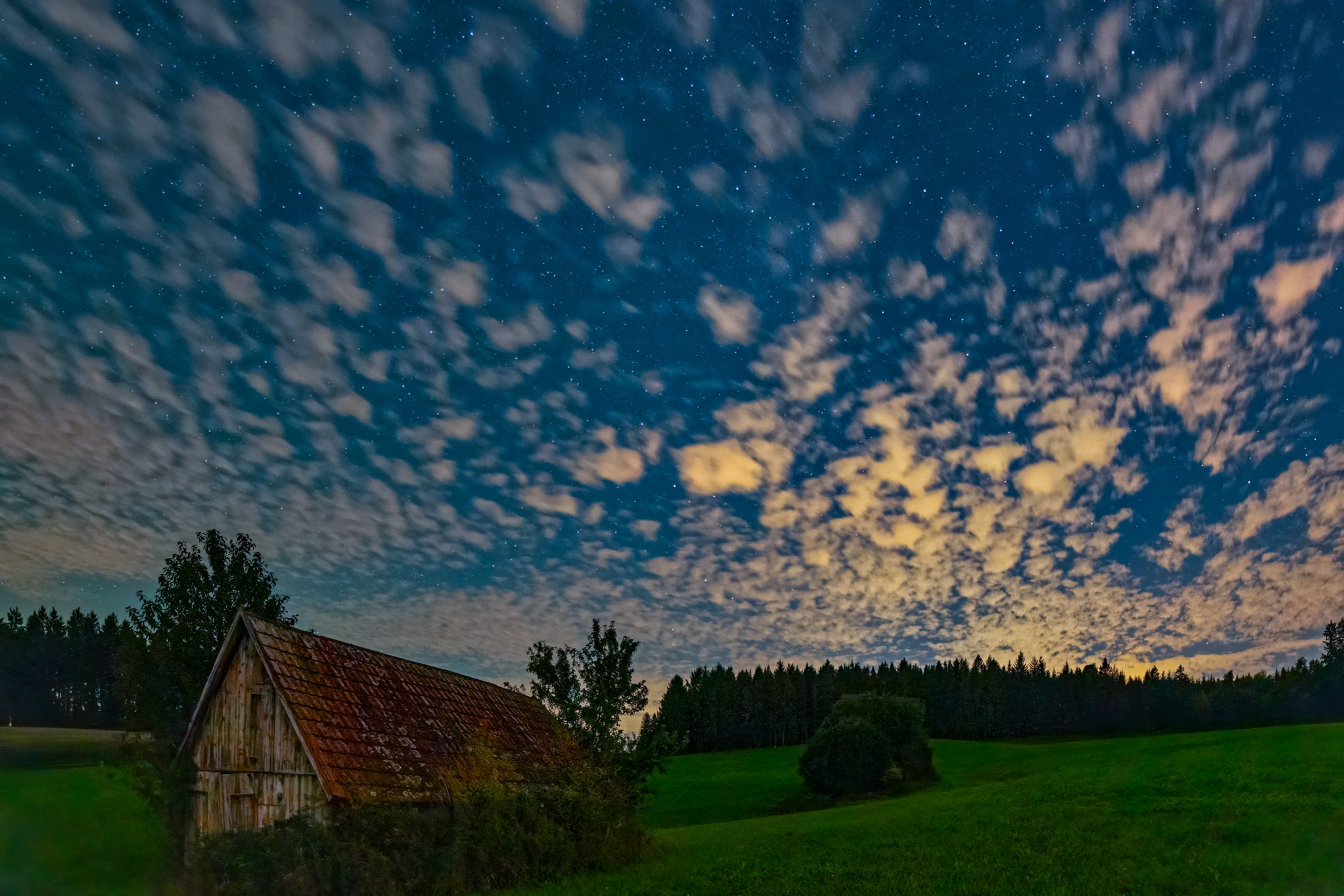 Sternenhimmel und leuchtende Wolken über alter Scheune